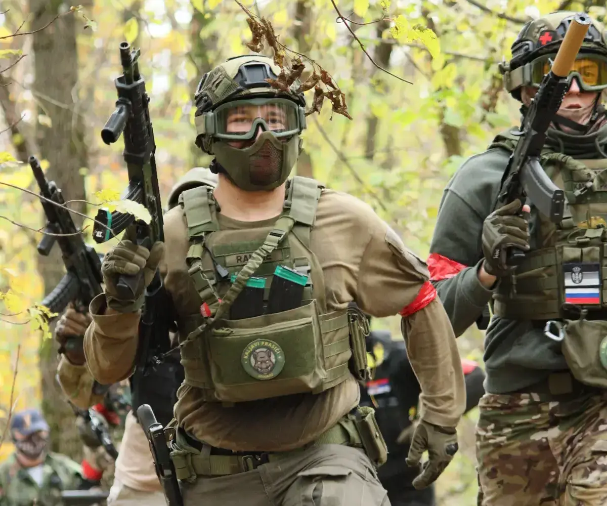 Airsoft igrač u šumi i vojnoj opremi u železniku leži na zemlji i drži airsoft repliku